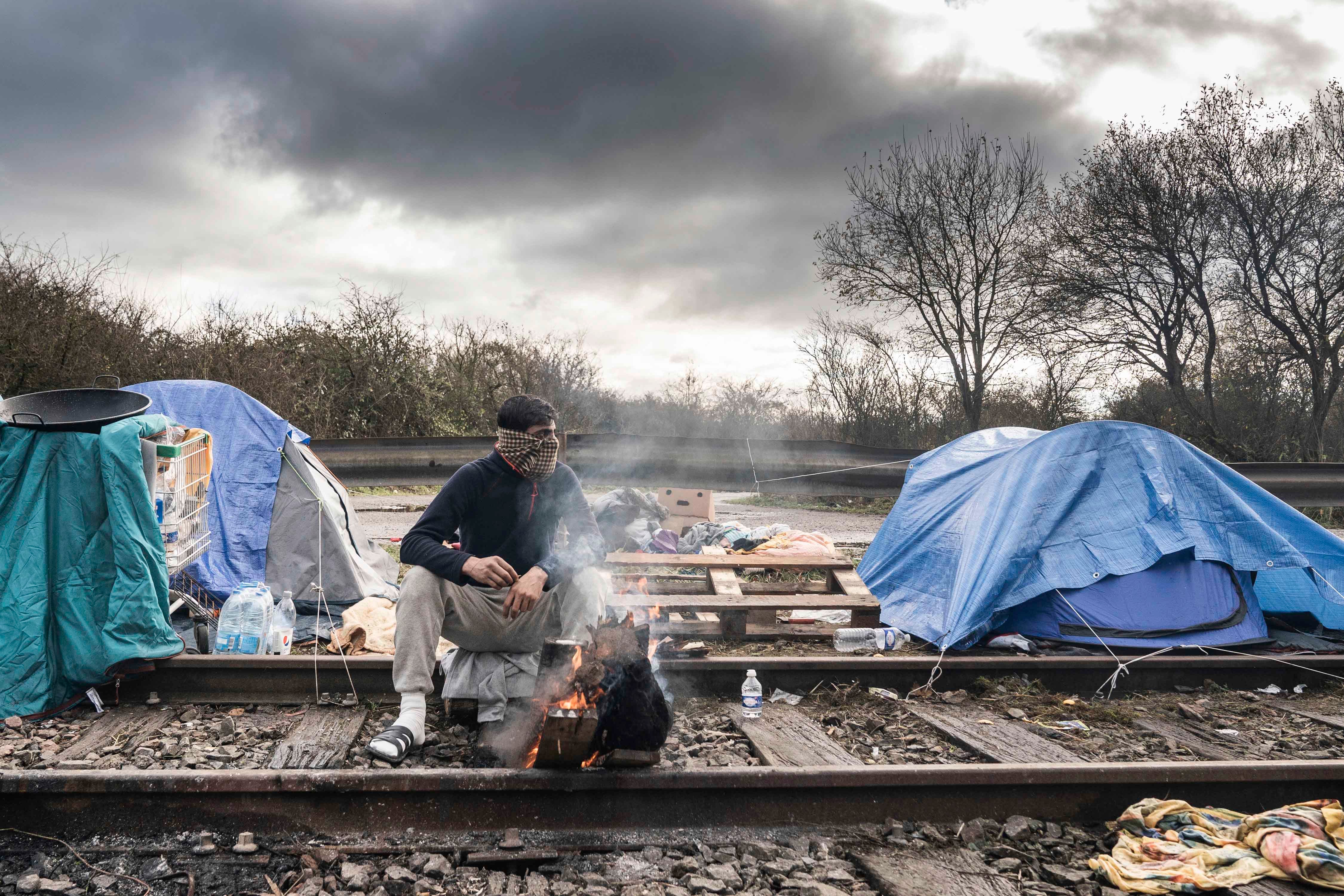 A migrant seen keeping himself warm by burning firewood at a makeshift migrant camp in the Dunkirk area of Northern France.