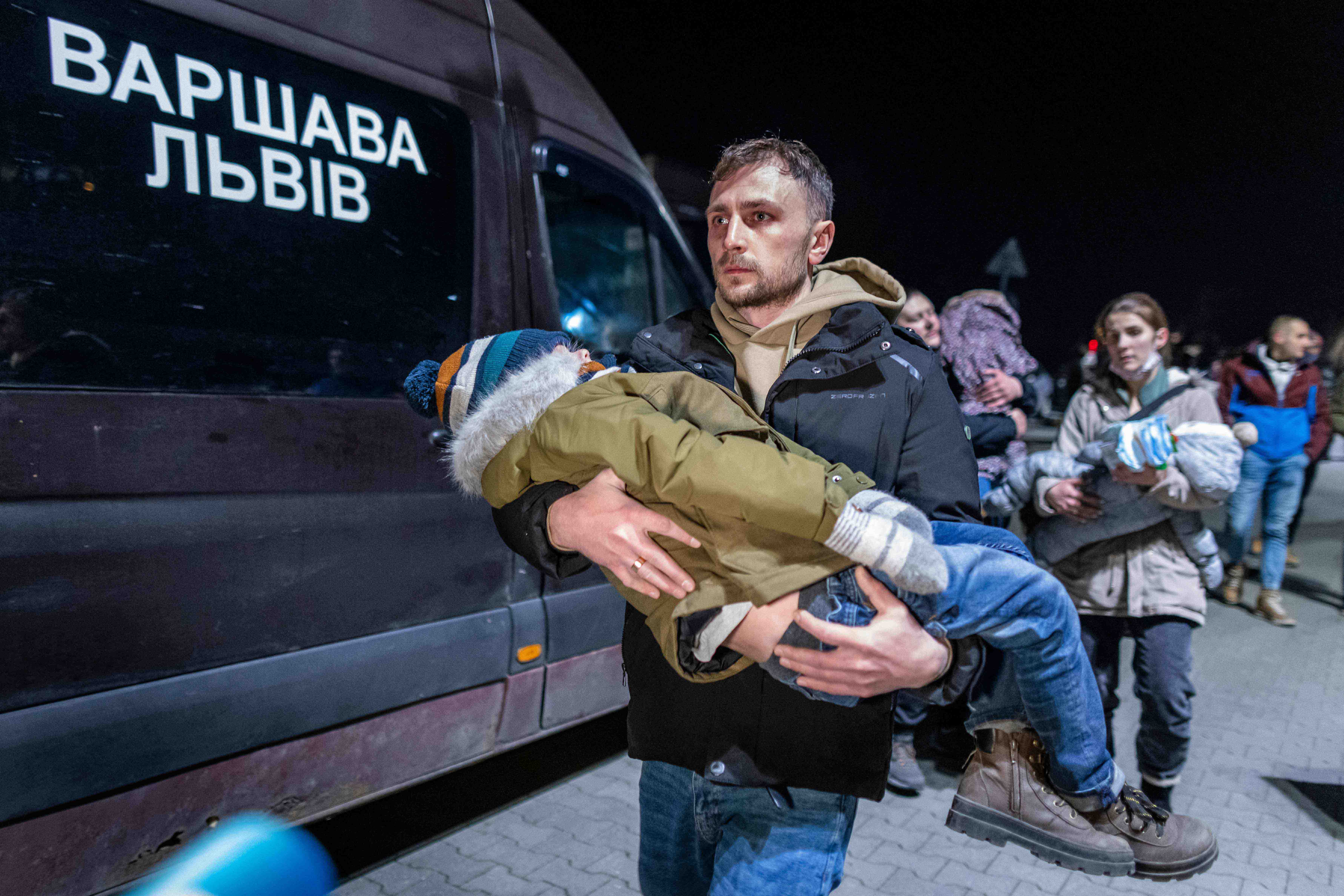 A volunteer carries a Ukranian child as civilians fleeing the conflict in Ukraine, arrive on buses in Przemsyl, eastern Poland, from the Medyka pedestrian border crossing.