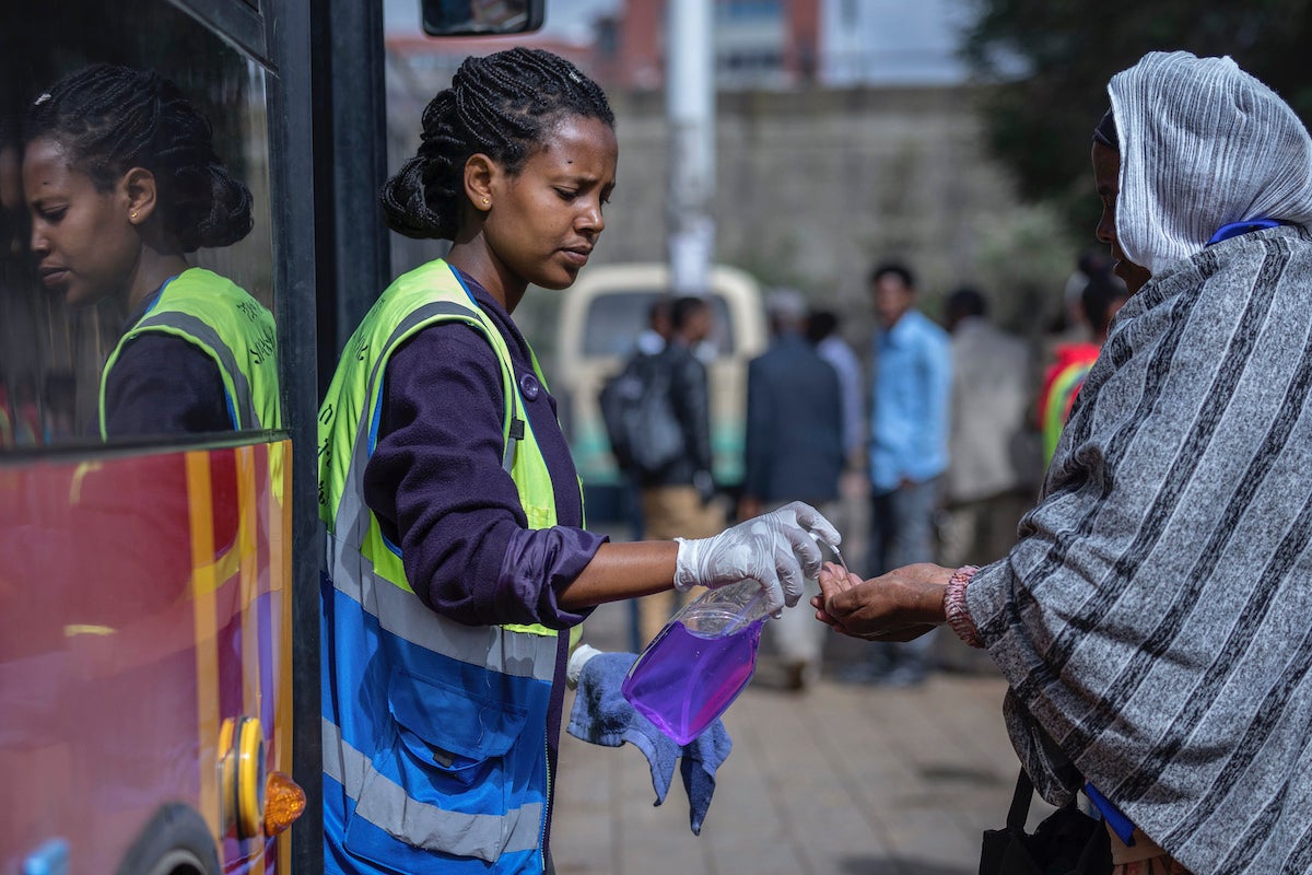 A volunteer provides hand sanitizer to passengers entering a bus