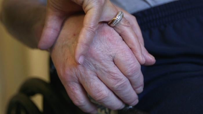 A nursing home resident holds his wife’s hand. 