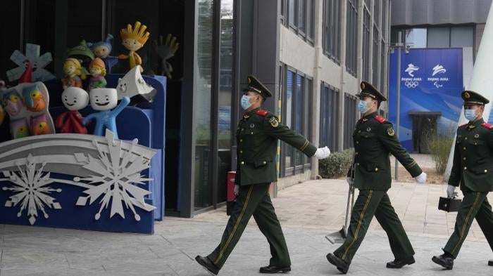 Chinese paramilitary police march past mascots from prior Winter Olympics displayed at Shougang Park in Beijing, China, January 21, 2022. © 2022 AP Photo/Ng Han Guan