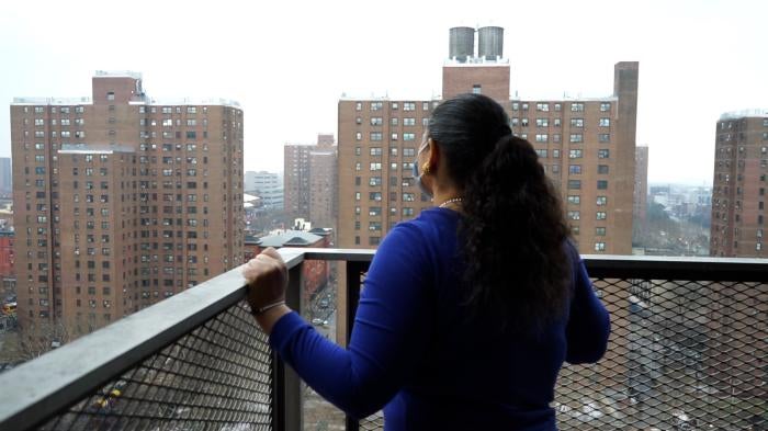Woman standing on balcony looking at public housing buildings.