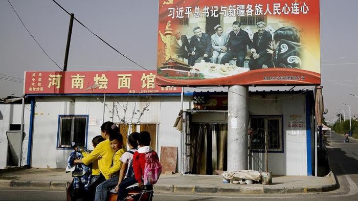 A Uighur woman picking up school children rides past a picture showing China's President Xi Jinping joining hands with a group of Uighur elders at the Unity New Village in Hotan, in western China's Xinjiang region. 