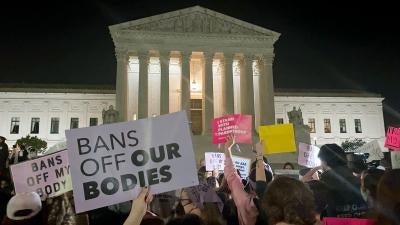 People protest holding signs outside of the US Supreme Court at night