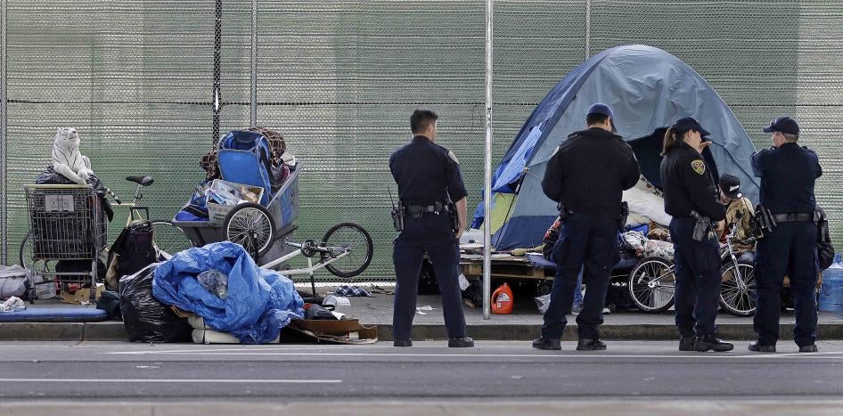 Police officers wait while people experiencing homelessness collect their belongings during a sweep of their encampment under a San Francisco, California freeway, March 1, 2016. 