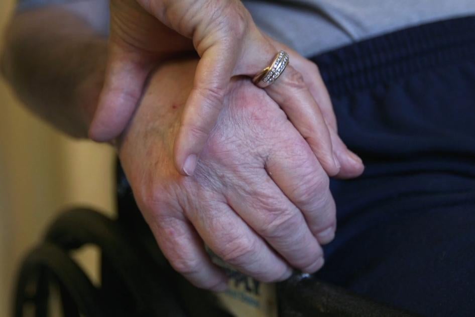 A nursing home resident holds his wife's hand.