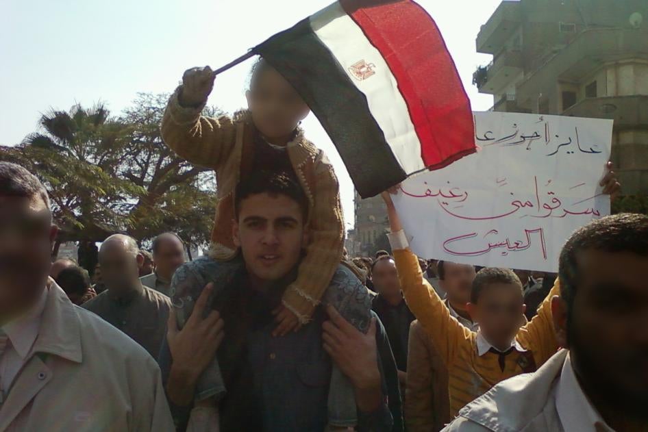A man stands in a protest with a child on his back waving the Egyptian flag