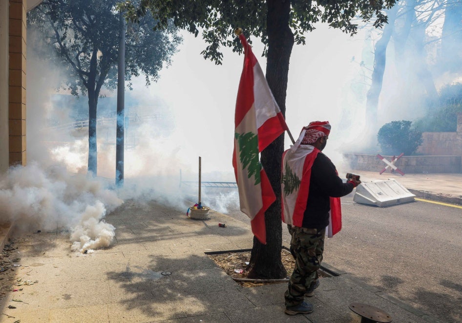 A demonstrator holds a Lebanese flag as he stands near smoke rising from tear gas during a protest over the deteriorating economic situation, at Riad al-Solh square in Beirut, Lebanon.