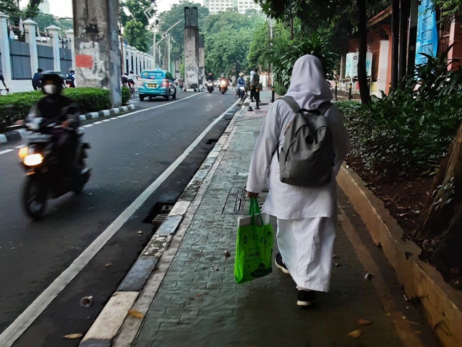 A schoolgirl walking near her state high school in Senayan, Jakarta, Indonesia. The mandatory school uniform includes a hijab, a long-sleeve shirt, and a long skirt.