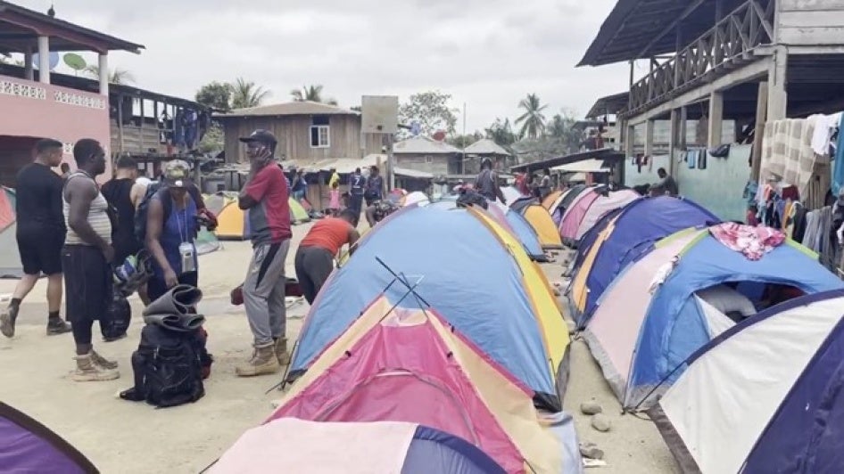 Migrants stand next to tents set up in a rural village 