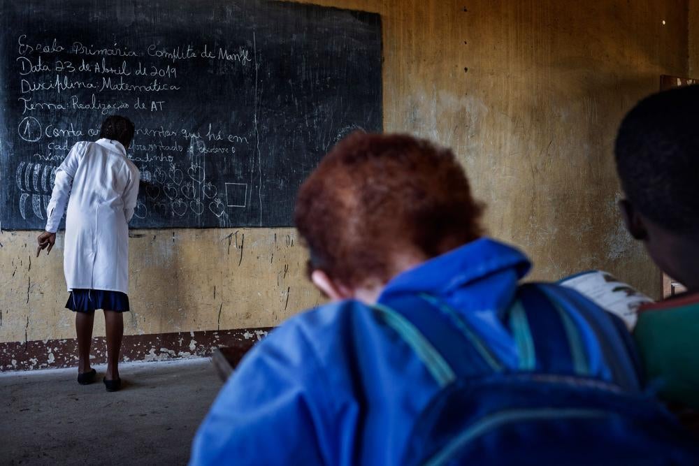 Josina, uma menina com albinismo, senta-se na frente da sala de aula no distrito de Chiuta, Moçambique. Josina recebe apoio de sua professora, no entanto crianças com albinismo costumam enfrentar vários obstáculos, incluindo bullying e falta de ajustes necessários na sala de aula.