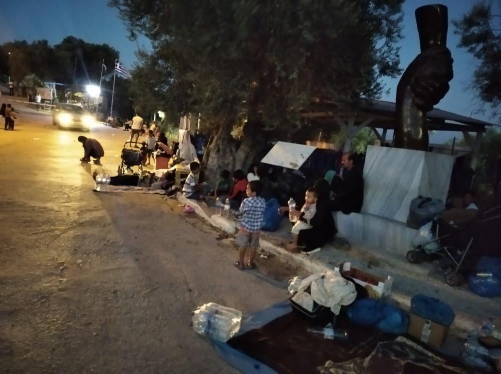 A family sits on a roadside at night with their possessions