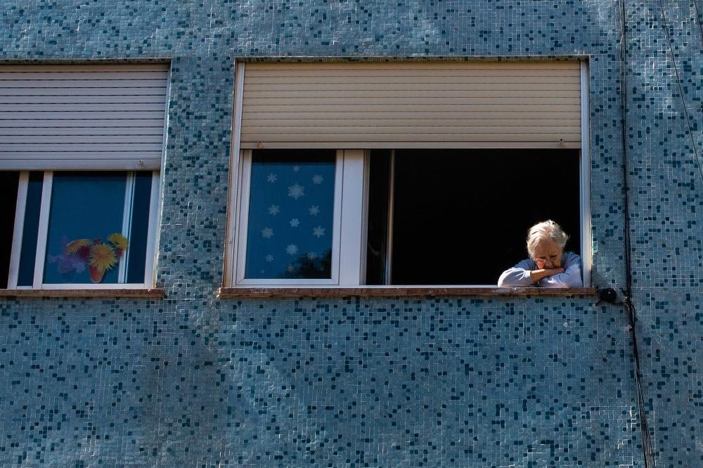 An elderly woman stares out of her apartment window