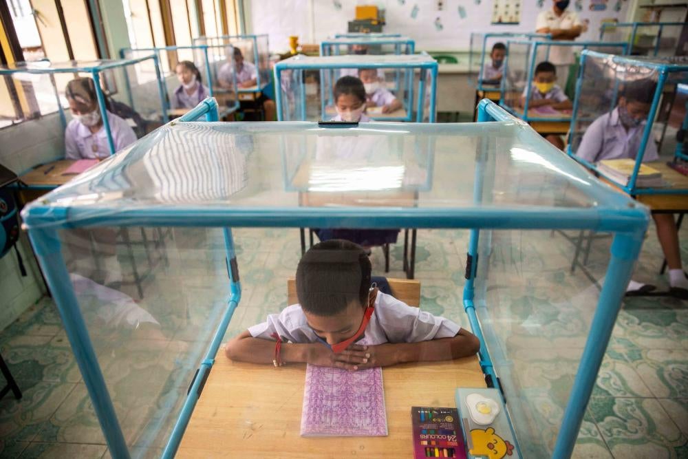 Children sit at desks enclosed with plastic screens in a classroom