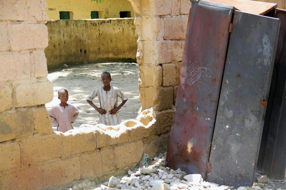 Des enfants regardent à travers un trou où se trouvait la fenêtre d’une salle de classe de l’école primaire Yerwa de Maiduguri dans l’État de Borno, détruite lors d’attaques menées par Boko Haram en 2010 et 2013. Construite en 1915, c’était la première éc