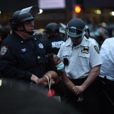 A Black woman in a mask is forcibly detained by two police officers
