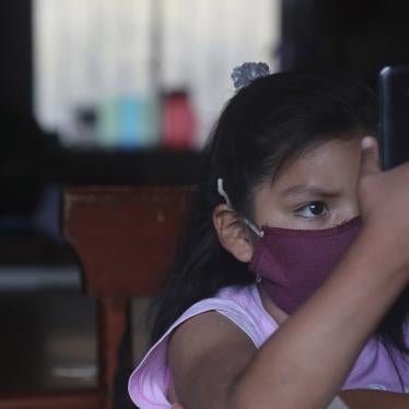 A young girl wearing a face mask holds up a cell phone