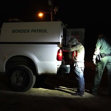 A man stands with his hands on the back of a van marked "Border Patrol"