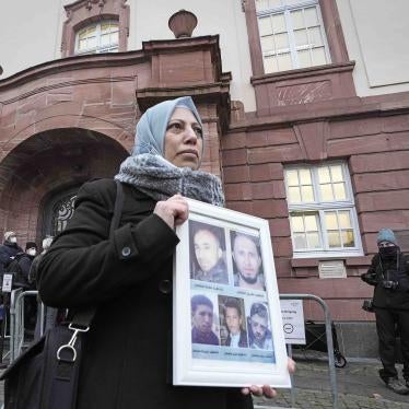 Yasmen Almashan from Syria holds a poster with pictures of her five brothers who died in Syria as she waits in front of the court in Koblenz, Germany