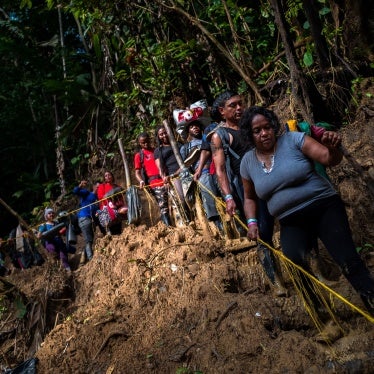Migrants and asylum seekers climb down a muddy hillside trail in the jungle