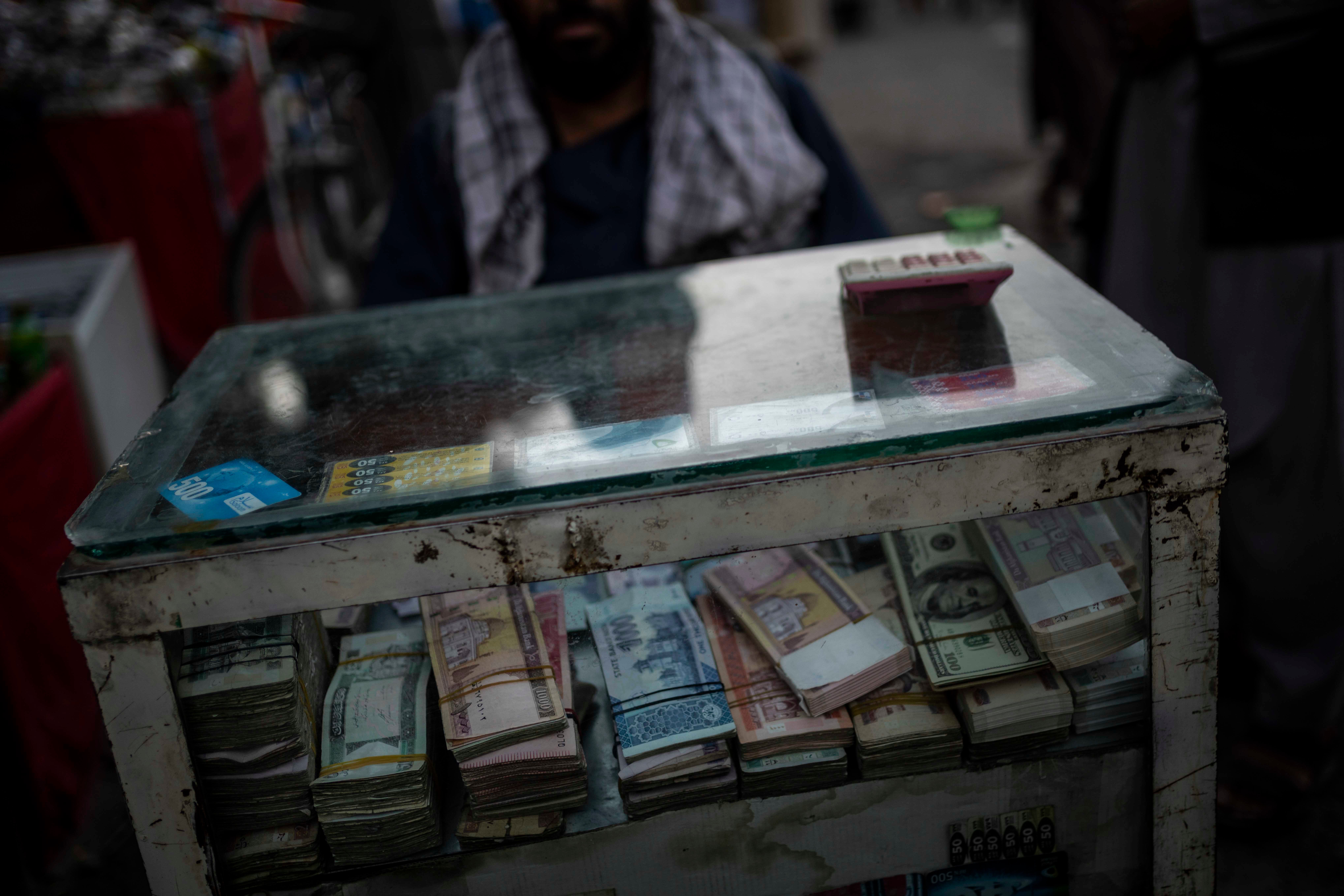 Uma pessoa sentada atrás de uma caixa com dinheiro a espera por clientes que precisem realizar câmbio na cidade velha de Cabul, Afeganistão, 14 de setembro de 2021. 