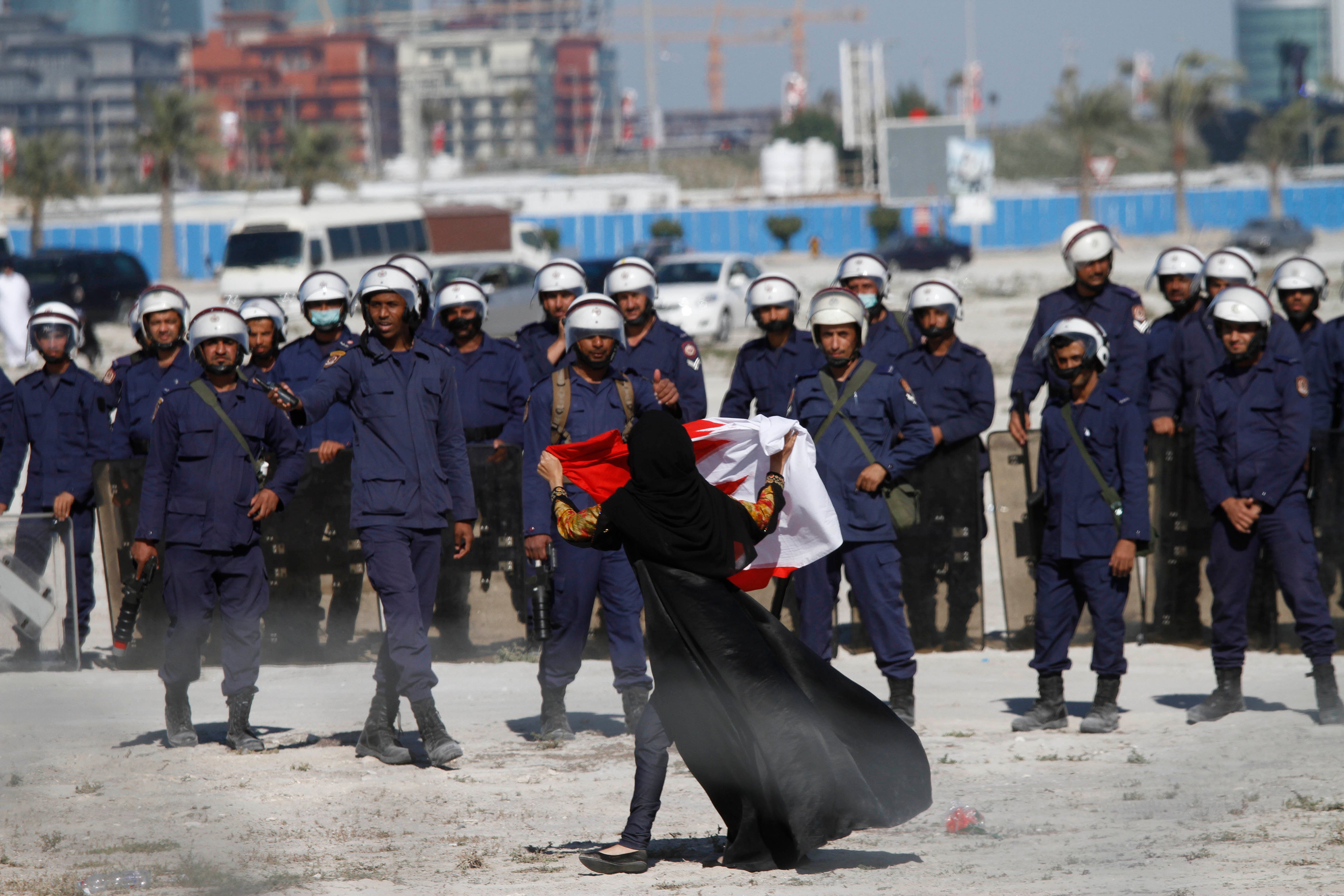 متظاهرة مناهضة للحكومة تلوح بالعلم بالبحريني أمام الشرطة بينما يحتل المتظاهرون دوار اللؤلؤة مجددا في 19 فبراير/شباط 2011 في المنامة، البحرين. بعد مرور عشر سنوات على الاحتجاجات المناهضة للحكومة، سُحِقت جميع أشكال المعارضة تقريبا.