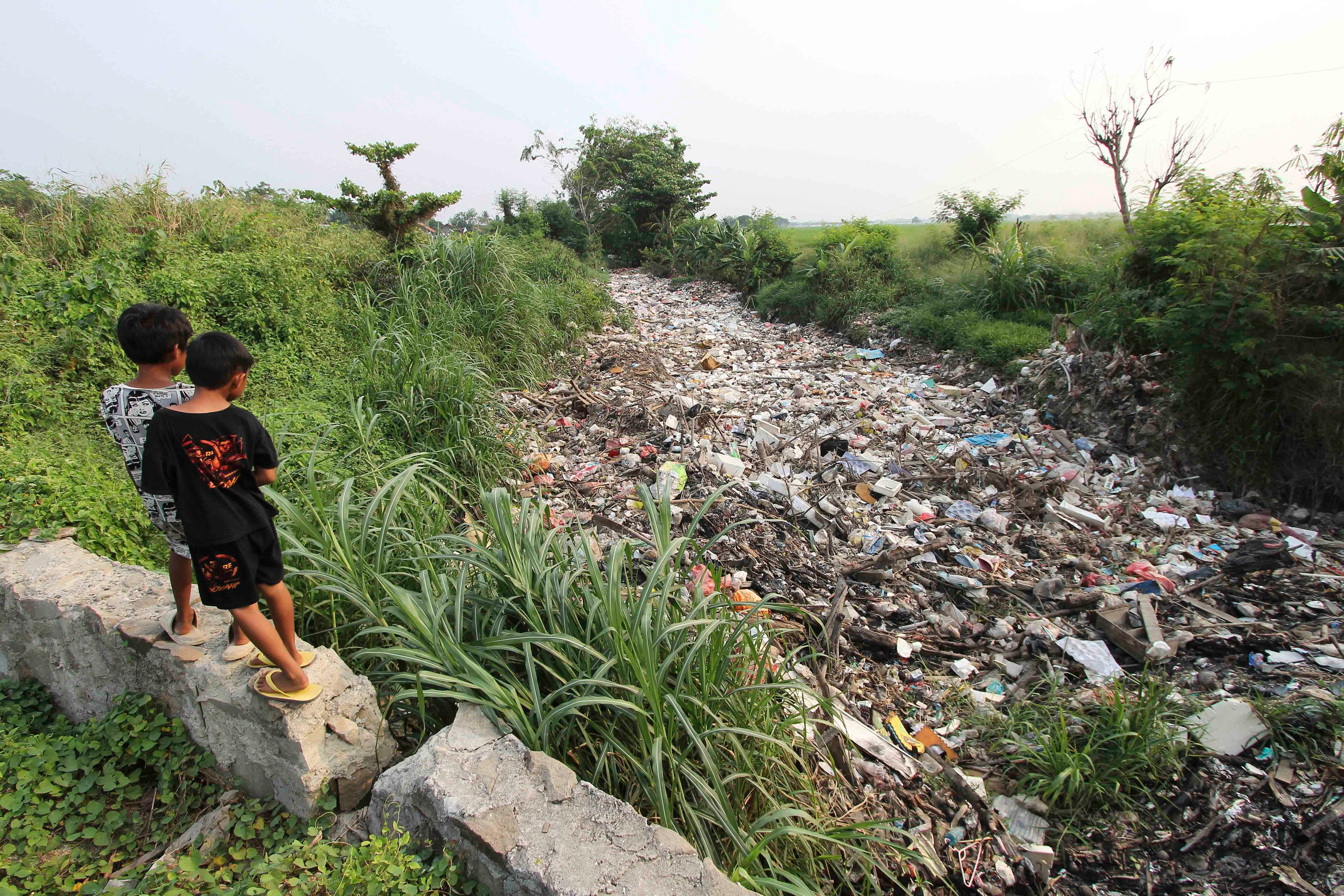 Two children stand above a river filled with garbage 