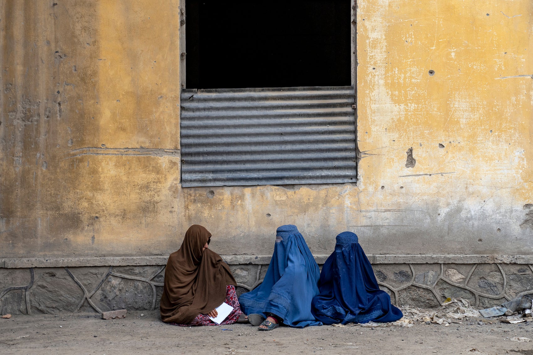 Trois femmes afghanes assises devant un immeuble à Kaboul, en Afghanistan, attendaient la distribution de rations alimentaires par un groupe d'aide humanitaire, le 23 mai 2023. 