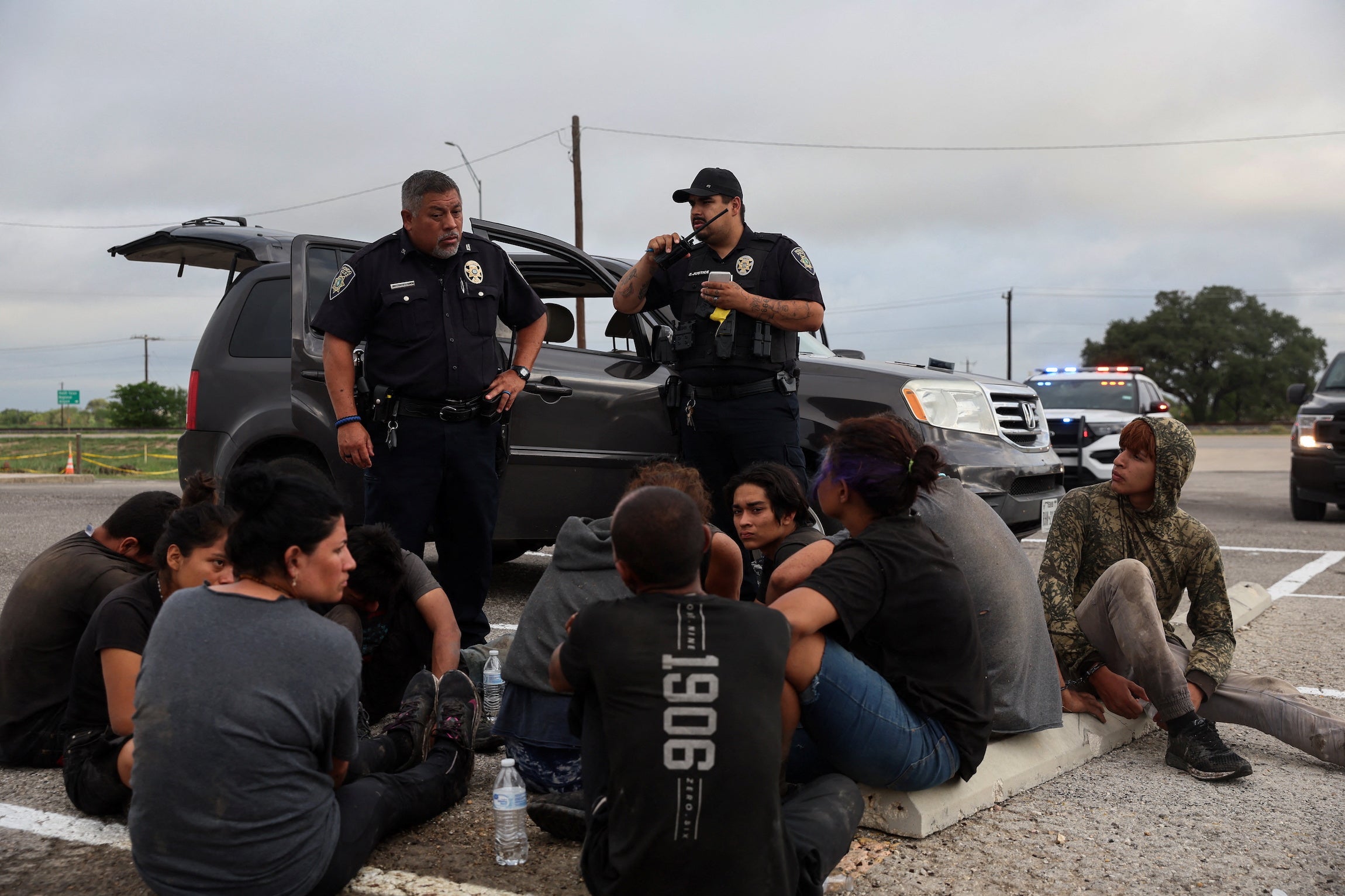 Asylum seekers from Central America sit by the road after police detained them in Hondo, Texas, about 100 miles from the US-Mexico border, June 1, 2022. 