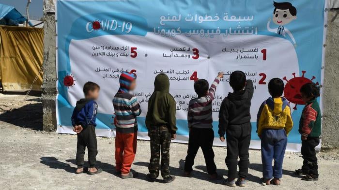 Displaced Syrian children read a poster, outlining 7 steps to prevent the spread of COVID-19 coronavirus disease, at a camp for the internally displaced near Dayr Ballut, near the Turkish border in the rebel-held part of Aleppo province on March 22, 2020, during a campaign to prevent the spread of the virus.