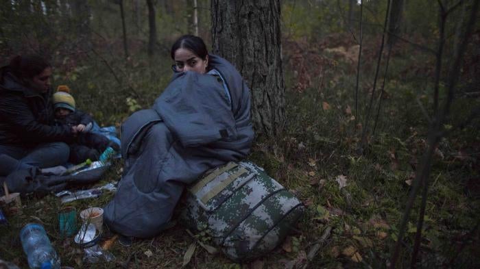 Two women and a child huddle in sleeping bags on the forest floor after crossing the Polish-Belarusian border near Michalowo on October 6, 2021.
