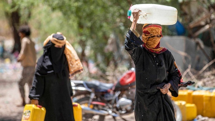 Women walk with canisters filled with water from a tanker truck on the outskirts of Taizz.