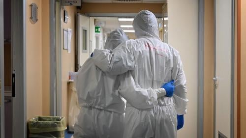 Two medical workers in scrubs embrace in a hospital hallway
