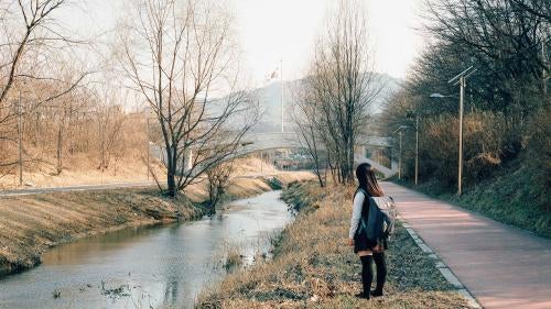 A schoolgirl stands next to a stream 