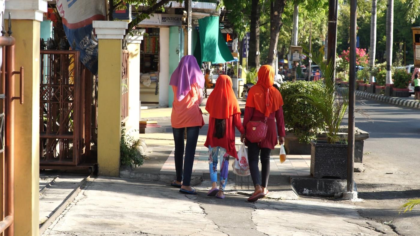 Three girls in hijabs are walking away from the camera down a street in Indonesia