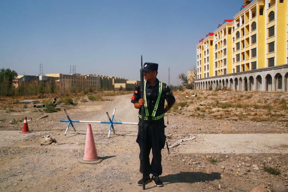 An armed police officer stands on a road leading towards a large yellow building