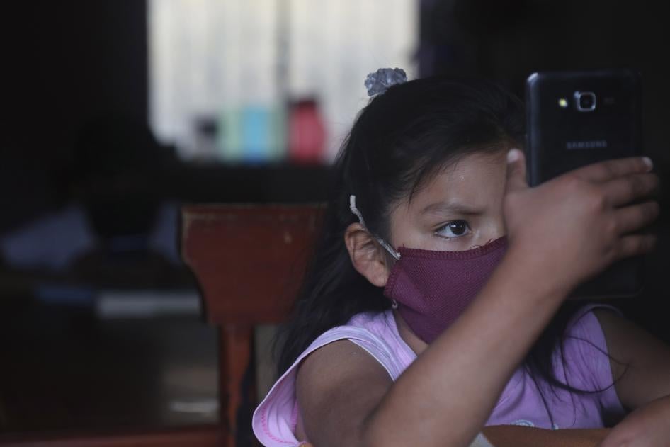 A young girl wearing a face mask holds up a cell phone