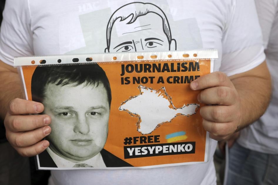 A man holds a placard that says "Journalism is Not a Crime" and "#FreeYesypenko"
