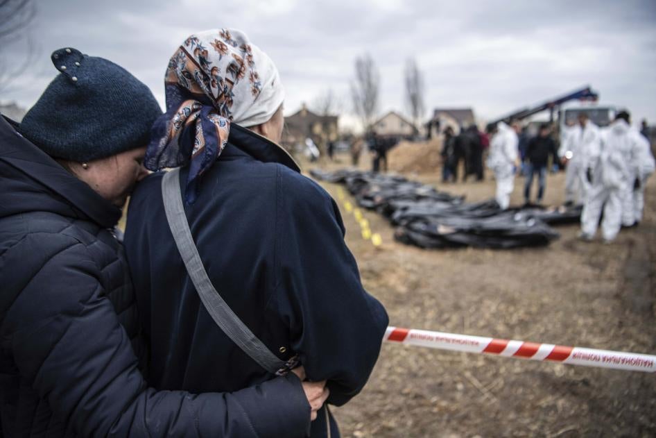 Women watch and embrace each other as bodies are exhumed from a mass grave by the authorities