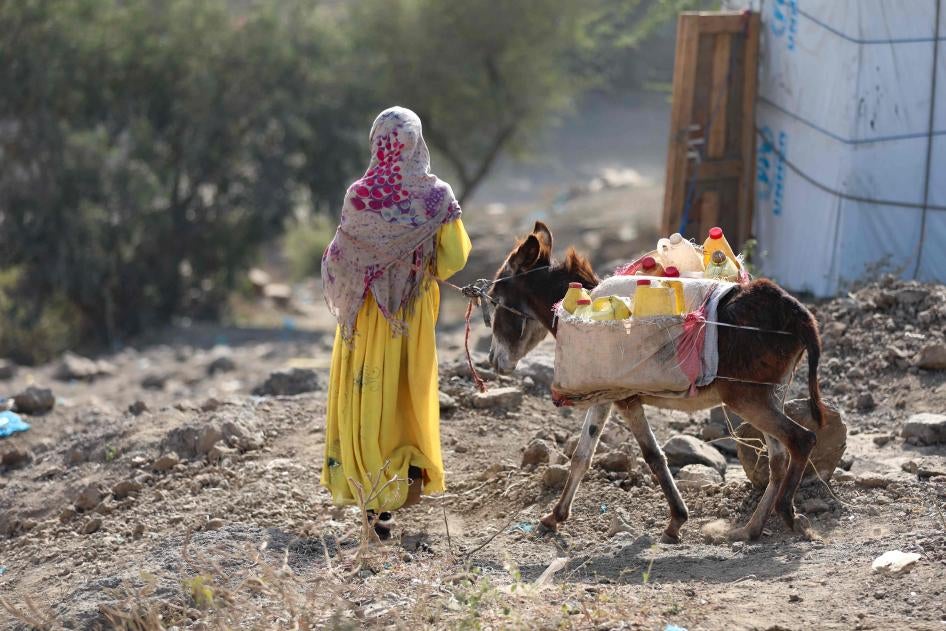 Une jeune fille marche aux côtés d'un âne transportant des récipients d'eau.