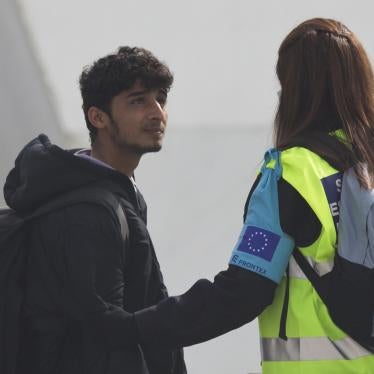 An officer from the European Union’s border protection agency, Frontex, holds the arm of a migrant as they board a ferry in the port of Mytilini, Lesbos island, Greece, on Friday, April 8, 2016.