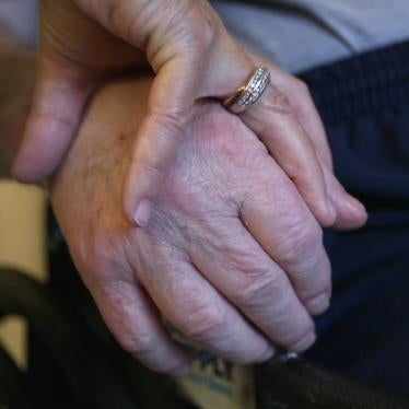 A nursing home resident holds his wife’s hand. 