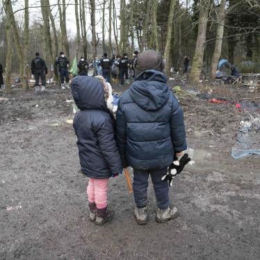 Two children wearing winter coats stand in a forest in front of a group of police officers