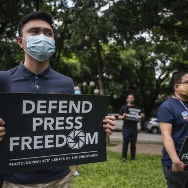 People in face masks hold signs that read "Defend Press Freedom"