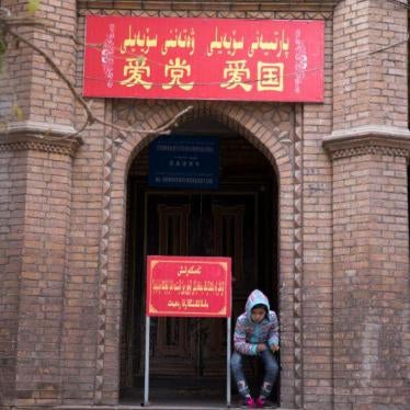 A child rests near the entrance to a mosque, where a banner reads "Love the party, Love the country" in the old city district of Kashgar in western China's Xinjiang region, November 4, 2017. © 2017 AP Photo/Ng Han Guan