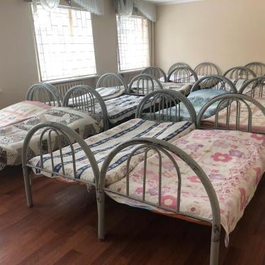 Sixteen beds fill a room with barred windows in a closed institution for children with disabilities.