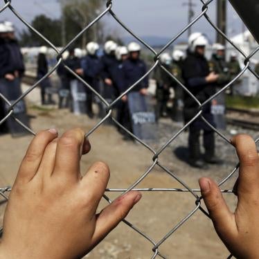A child places his hands on a fence as Greek police officers stand guard at a makeshift camp for migrants and refugees in Greece.